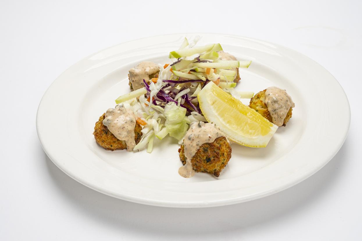 Crab cakes with sauce plated alongside greens and a lemon wedge.